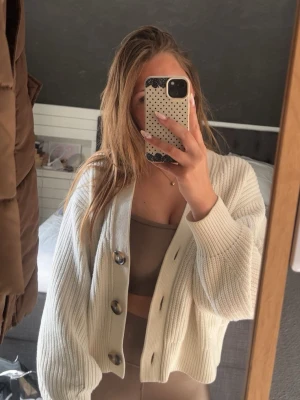 Vit ribbstickad kofta med stora knappar från hm - Snygg vit kofta i ribbstickat material med oversized passform och stora, dekorativa knappar framtill. Koftan har långa ärmar och en kortare, boxig modell som ger en trendig look. Perfekt att slänga över ett linne eller topp.