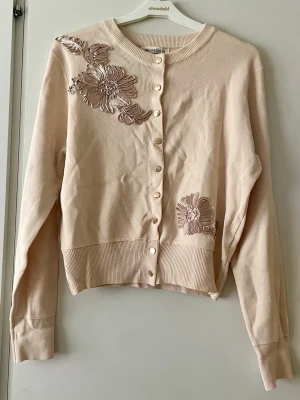 *NY*LjusBeige 3Dkofta med blommiga detaljer stl M/L - Ny med lapp fr J&H fashion Paris  Står stl L/XL, enligt mig sitter den bäst på en  M/L(40/42). Ljusbeige/vanilj med guldknappar och 3D blommor i blankt tyg.  Lite kortare i modellen,  material: 50,7% viskos, 28,6% polyester, 20,7% nylon. Längd: ca 53 cm, Byst: ca 76 cm.   Nypris: 499 sek, Pris nu: 299 sek  #3Dsweater #ljusbeige #stl4042 #nwt #trending #guldknappar #summer #paris