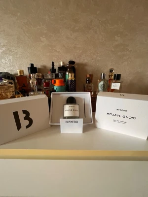 Byredo Mojave Ghost Eau de Parfum - Byredo Mojave Ghost Eau de Parfum kommer i en stilren, rund glasflaska med svart rund kork och vit etikett. Doften är unisex och flaskan har en minimalistisk design som känns lyxig och modern. Perfekt för dig som gillar exklusiva parfymer med unik karaktär.