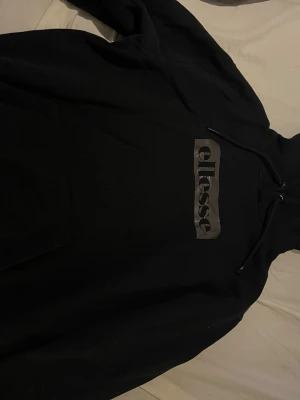 Svart Ellesse hoodie med logga - Snygg svart hoodie från Ellesse med stor logga i grått på bröstet. Klassisk modell med huva och dragsnören. Finns byxor om man vill köpa till det.