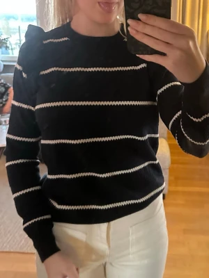 Svartvit randig stickad tröja - Svart stickad tröja med vita horisontella ränder och puffade axlar. Tröjan har rund halsringning och långa ärmar. Perfekt för dig som gillar en klassisk men trendig look.