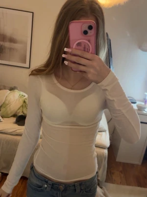 Vit långärmad topp i stretchigt material - Snygg vit långärmad topp med rund halsringning och figurnära passform. Tillverkad i ett stretchigt och tunt material som sitter tight mot kroppen. Perfekt att styla med jeans eller kjol för en enkel och fräsch look 