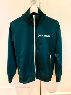 👉 Palm Angels Track Jacket S – Nyskick – Nypris 8357kr 🔥 - Säljer en riktigt snygg och eftertraktad jacka från Palm Angels i mörkgrön färg med stilrena vita detaljer. Perfekt för både vardag och en mer uppklädd streetwear-look.  ✨ Storlek: S ✨ Skick: Kanonskick – inga fläckar eller skador ✨ Inköpt: 2023-09-28 via Farfetch ✨ Nypris: 8357 kr ✨ Jag betalade: 6093 kr (kvitto finns och skickas vid intresse) ✨ Djur- och rökfritt hem  Jackan har en hög krage, hel dragkedja och diskret logotyp på bröstet – en tidlös modell som alltid håller stilen. 