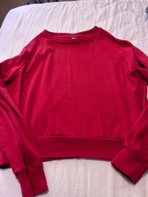 Röd sweatshirt från BikBok - En enkel och snygg röd sweatshirt från BikBok med rund halsringning och långa ärmar. Tröjan har breda muddar vid ärmslut och nederkant. Tillverkad i mjukt material som känns skönt mot huden. Perfekt för en avslappnad och trendig look.