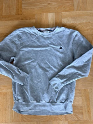 Grå sweatshirt från U.S. Polo Assn. - Klassisk grå sweatshirt från U.S. Polo Assn. med rund halsringning och broderad logga på bröstet. Tröjan har långa ärmar, ribbade muddar och är tillverkad i mjuk bomullsblandning. Perfekt för en avslappnad och stilren look. Öppen för pris förslag och frågor! 😁🙌🤝👔