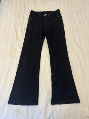 Svarta bootcut jeans med utsvängda ben - Snygga svarta bootcut jeans med klassisk femficksdesign och utsvängda ben. Jeansen har normal midja och stängs med knapp och dragkedja. Perfekta för dig som gillar en retroinspirerad look och vill ha ett par jeans som sticker ut.