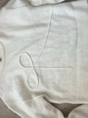 Vit stickad tröja från H&M - Säljer en vit stickad tröja från H&M med ett unikt broderat snörmönster framtill. Tröjan har rund halsringning, ribbade muddar och är gjord i ett mjukt material som känns skönt mot huden.