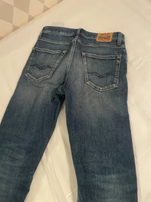 Blå raka jeans från Replay - Säljer ett par klassiska blå jeans från Replay med raka ben och snygg slitning. Jeansen har fem fickor, tydliga sömmar och läderpatch bak i midjan. Perfekta för dig som gillar en avslappnad men stilren look. Modellen heter Thad. Skriv gärna frågor!😃