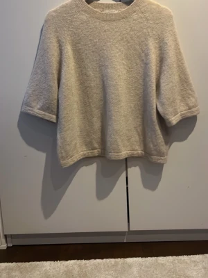 Beige stickad tröja & Other Stories - Mysig beige stickad tröja från & Other Stories med rund halsringning och halvlånga ärmar. Tröjan har en avslappnad passform och är tillverkad i ett mjukt, luddigt material som känns lyxigt och skönt.