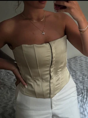 Grön satin korsett med dragkedja - Stilren beige korsett i satin med markerade sömmar och dragkedja framtill. Axelbandslös design som ger en snygg siluett och passar perfekt till både byxor och kjol. Ger en trendig och elegant look. Kolla min profil för fler plagg! 🥰
