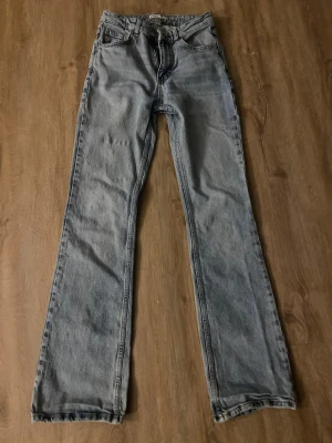 Ljusblå jeans - Säljer ett par ljusblå bootcut jeans med klassisk femficksdesign och hög midja. Jeansen har en avslappnad passform och raka ben som går ut lite nedtill. Perfekta för en trendig och avslappnad look.