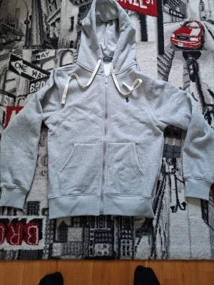 Grå hoodie från Polo Ralph Lauren - Snygg grå zip hoodie från Polo Ralph Lauren. Den är i väldigt bra skick. Den passar tyvär inte mig så bra så jag säljer den. 