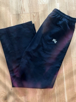 Svarta mjukisbyxor från NC - Säljer ett par svarta mjukisbyxor från NC med en ficka bak och broderad logga. Byxorna har resår i midjan och är gjorda i mjukt material som känns skönt mot huden. Perfekta för chill dagar eller när du vill ha det bekvämt.