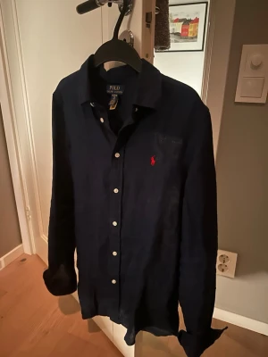 Mörkblå linneskjorta från Polo Ralph Lauren - Snygg mörkblå skjorta från Polo Ralph Lauren i linne med klassisk krage och vita knappar. Ikoniska röda logotypen broderad på bröstet. Perfekt för dig som gillar stilrena och tidlösa plagg. Skjortan är i nyskick och har knappt används, kom privat vid flera frågor!😀