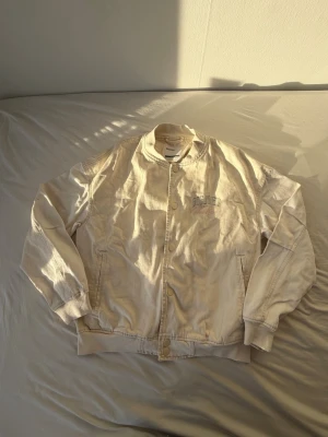 jeansjacka från Bershka - Snygg vit jeansjacka från Bershka med broderad text på bröstet. Jackan har ribbade muddar, knappstängning och två fickor framtill. Perfekt för dig som vill ha en stilren och trendig look. Aldrig använt.