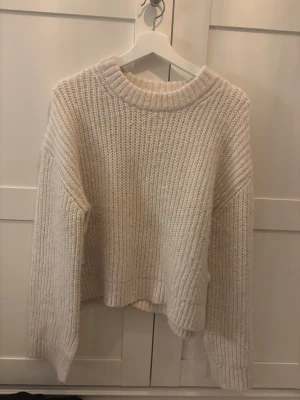 Beige chunky stickad tröja - Mysig beige stickad tröja med grov ribbstickning och avslappnad passform. Tröjan har rund halsringning, långa ärmar och breda muddar vid ärmslut och nederkant. Perfekt för lager på lager under kyliga dagar.