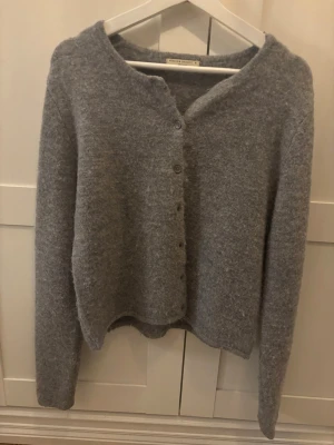 Grå kofta från Gina Tricot - Mysig grå kofta från Gina Tricot i borstat material. Koftan har rund halsringning, knäppning framtill med matchande knappar och långa ärmar. Perfekt för lager på lager och enkel att styla till olika outfits.