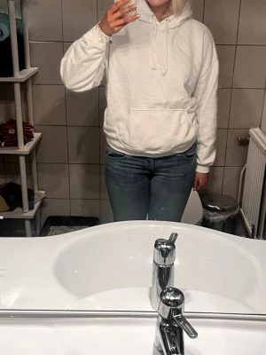 Vit hoodie med huva och magficka - Säljer en enkel och clean vit hoodie med huva och dragsko. Hoodien har en stor magficka framtill och ribbade muddar vid ärmslut och nederkant. Perfekt för chill dagar eller när du vill ha en basic look. Materialet känns mjukt och bekvämt mot huden.