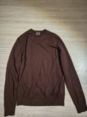 Brun merinoulltröja från H&M - Mörkbrun stickad tröja från H&M i mjuk merinoull. Klassisk rund halsringning och långa ärmar. Perfekt för lager på lager och enkel att matcha med olika outfits.