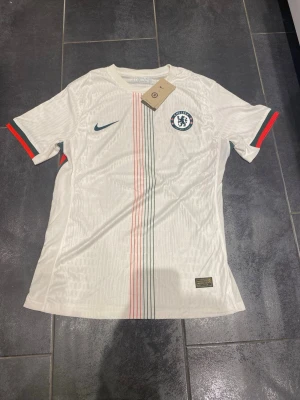 Chelsea Jersey vit - Hej! Jag säljer en jättefin Chelsea tröja. Jag fick den i julklapp, men den passar tyvärr inte mig, så jag tänker sälja den.