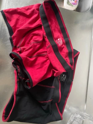 2-pack kalsonger från Uniqlo röd/svart - Två par kalsonger från Uniqlo i boxermodell. Ena paret är rött med svarta detaljer och det andra är svart med röda sömmar. Båda har bred resår i midjan och är tillverkade i mjuk bomullsblandning för skön passform.