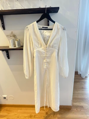 Vit långklänning från Gina Tricot - Vit långklänning från Gina Tricot med v-ringning och knappar framtill. Klänningen har dubbel ty så den blir inte genomskinlig. Bra skick men finns en rosa fläck på undertyget, alltså ingenting som syns!