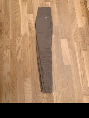 Bruna seamless tights från Gymshark - Säljer ett par bruna seamless tights från Gymshark med hög midja och diskret mönster längs benen. Tightsen har en tight passform och är perfekta för träning eller gymmet. Materialet är stretchigt och bekvämt för maximal rörelsefrihet.