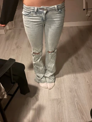 Ljusblå  bootcut jeans med låg midja och hål - Säljer ett par super fina lågmidjade ljusblå bootcut jeans med slitningar över knäna. Längst ner på byxan finns ytterst slit pga längden, skickar bild vid intresse! Även en tråd som sticker ut som på bilden, inget man ser vid användning💞