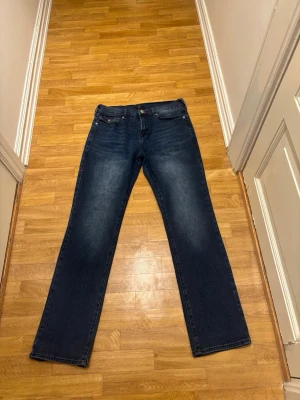True religion jeans - Snygga mörkblå jeans från true religion med raka ben och klassisk femficksmodell. Jeansen har röda sömmar vid fickor och midja som ger en cool detalj. Tillverkade i denim med en skön passform och dragkedja framtill.