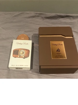Lattafa Vintage Radio Eau de Parfum - Lattafa Vintage Radio Eau de Parfum kommer i en snygg brun och guld förpackning med en unik flaska som liknar en retro radio. Flaskan har runda former och detaljer i bronsfärg. Doften är på 100 ml och passar dig som gillar exklusiva och kreativa parfymer.