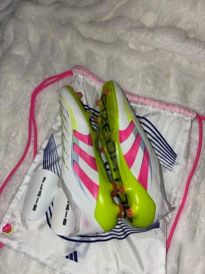 Adidas Predator fotbollsskor vit/rosa - Säljer ett par Adidas predator i storleken 45 skicket är som nytt nypris är 3299 skorna är både sköna och lätta, de är för spel på konstgräs (använda ett fåtal gånger) (benskydden ingår)