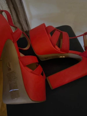 Röda platåpumps från Steve Madden - Snygga röda pumps med platå och bred klack från Steve Madden. Skorna har remmar med knutdetalj framtill och justerbart spänne vid ankeln.