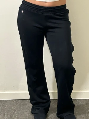Svarta mjukisbyxor från Champion - Svarta mjukisbyxor från Champion med rak passform och resår i midjan. Byxorna har en liten Champion-logga vid höften. 