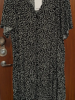 Svart blommig klänning från Monki - Svart klänning från Monki med vitt blommönster. Klänningen har v-ringning, korta ärmar och en luftig passform.
