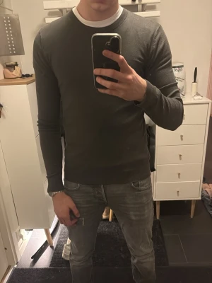 Mörkgrå stickad tröja - Snygg mörkgrå stickad tröja från Brothers med rund halsringning och långa ärmar. Tröjan har en smal passform och ribbade muddar vid ärmslut och nederkant. Perfekt att matcha med jeans eller chinos för en clean look.