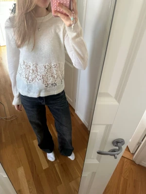 Vit tröja med spetsdetalj - Snygg vit tröja med lång ärm och bred spetsdetalj över magen. Tröjan har rund halsringning och är gjord i ett mjukt, stickat material. 