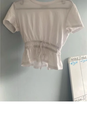 Vit croppad topp med knyt - Säljer en vit croppad topp med korta ärmar och knyt i midjan. Toppen har en avslappnad passform och är perfekt till jeans eller kjol. Tillverkad i mjukt bomullsmaterial för en skön känsla.