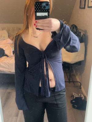 Mörkblå omlottopp med knyt - Trendig mörkblå omlottopp med knyt framtill och djup v-ringning. Långärmad modell med lite lösare passform i ärmarna. Perfekt för dig som vill ha en snygg och stilren topp till din garderob.