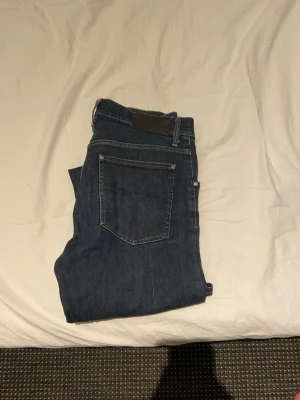 Mörkblå raka jeans - Snygga mörkblå jeans med klassisk femficksdesign och raka ben. Jeansen har en stilren look med diskreta sömmar och en svart patch bak i midjan. Perfekta för dig som gillar en enkel och tidlös stil.