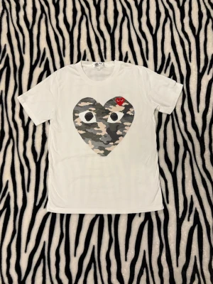 Comme des Garçons Play t-shirt - Vit t-shirt från Comme des Garçons Play med stort hjärta i camouflagemönster och ett litet rött! Står L i T-shirten men skulle säga M passar bättre, Påse o ett kort följer med! För bild med den på osv hör av dig 🤙 
