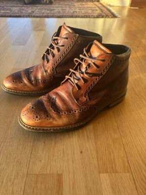 Bruna brogue-kängor i läder - Snygga bruna kängor i äkta läder med klassiskt broguemönster och snörning. Skorna har en robust sula och elegant design som passar perfekt till både jeans och kostymbyxor. Perfekta för dig som gillar tidlös stil med en twist.