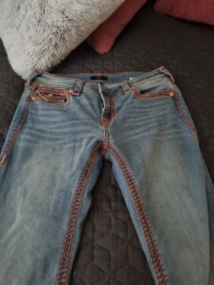 Jätte fin jeans från true religion jeans  - Unika blå jeans från true religion jeans med kontrasterande orange sömmar längs fickor, midja och ben. Klassisk femficksmodell med raka ben och låg midja. Jeansen har en cool vintagekänsla och detaljer som sticker ut. Perfekta för dig som vill ha något annorlunda i garderoben. Storlek 31 i väldigt fin skick använd en gång. 