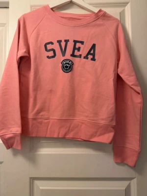 Rosa sweatshirt från Svea - Rosa sweatshirt från Svea med tryckt logga och emblem på bröstet. 