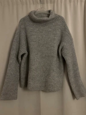 Grå stickad polotröja - Mysig grå stickad tröja med ribbad struktur och hög polokrage. Tröjan har en avslappnad passform och långa ärmar, perfekt för kyliga dagar. Materialet känns mjukt och värmande. Kommer inte ihåg vart den är köpt, skulle gissa på new yorker. 