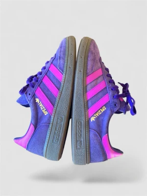 Adidas SPEZIAL lila/rosa sneakers - Säljer ett par Adidas SPEZIAL sneakers i lila mocka med rosa detaljer och klassiska tre ränder på sidorna. Skorna har grå sula och gula SPEZIAL-loggor på sidan. Perfekta för dig som vill sticka ut med färg och stil. Normal passform