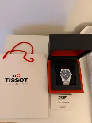 Tissot PRX silverfärgad klocka - Stilren Tissot PRX klocka med blå urtavla och silverfärgat armband i rostfritt stål. perfekt för dig som gillar en simpel men snygg klocka. Levereras i original låda med tillhörande manual. ÖPPEN FÖR BYTEN