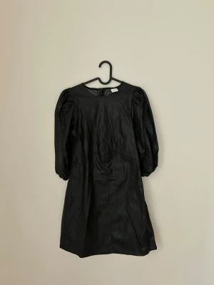 Svart kort klänning med puffärm - Säljer en svart kort klänning med puffiga trekvartsärmar och rund halsringning. Klänningen har en snygg struktur och är tillverkad i ett skinnliknande material 