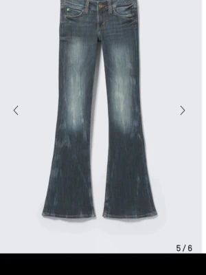 Blå bootcut jeans med slitningar - Snygga blå bootcut jeans med slitningar och lätt tvättad look. Jeansen har låg midja, klassiska fem fickor och vida ben. Perfekta för en avslappnad och trendig stil. Storlek 28/34