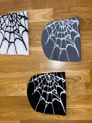 Mössa med spindelnätsmönster - Cool mössa i mjukt stickat material med spindelnätsmönster. Finns i svart, vitt och grått med kontrasterande vitt eller svart mönster. Perfekt för dig som gillar alternativ stil eller vill sticka ut lite extra. Materialet känns stretchigt och bekvämt.