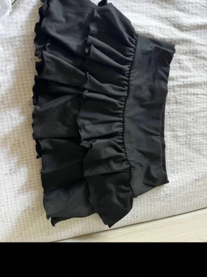 Svart volangskort kjol - Supersöt svart kjol med volanger och låg midja.  I kjolen är det inbyggda shorts 